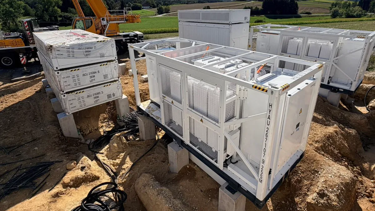 Batteriespeichermodule auf ihren Fundamenten während der Errichtung, im Hintergrund ein Kran